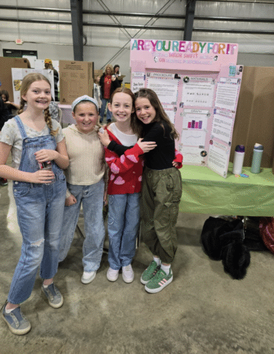 Four smiling students stand in front of a science fair display.